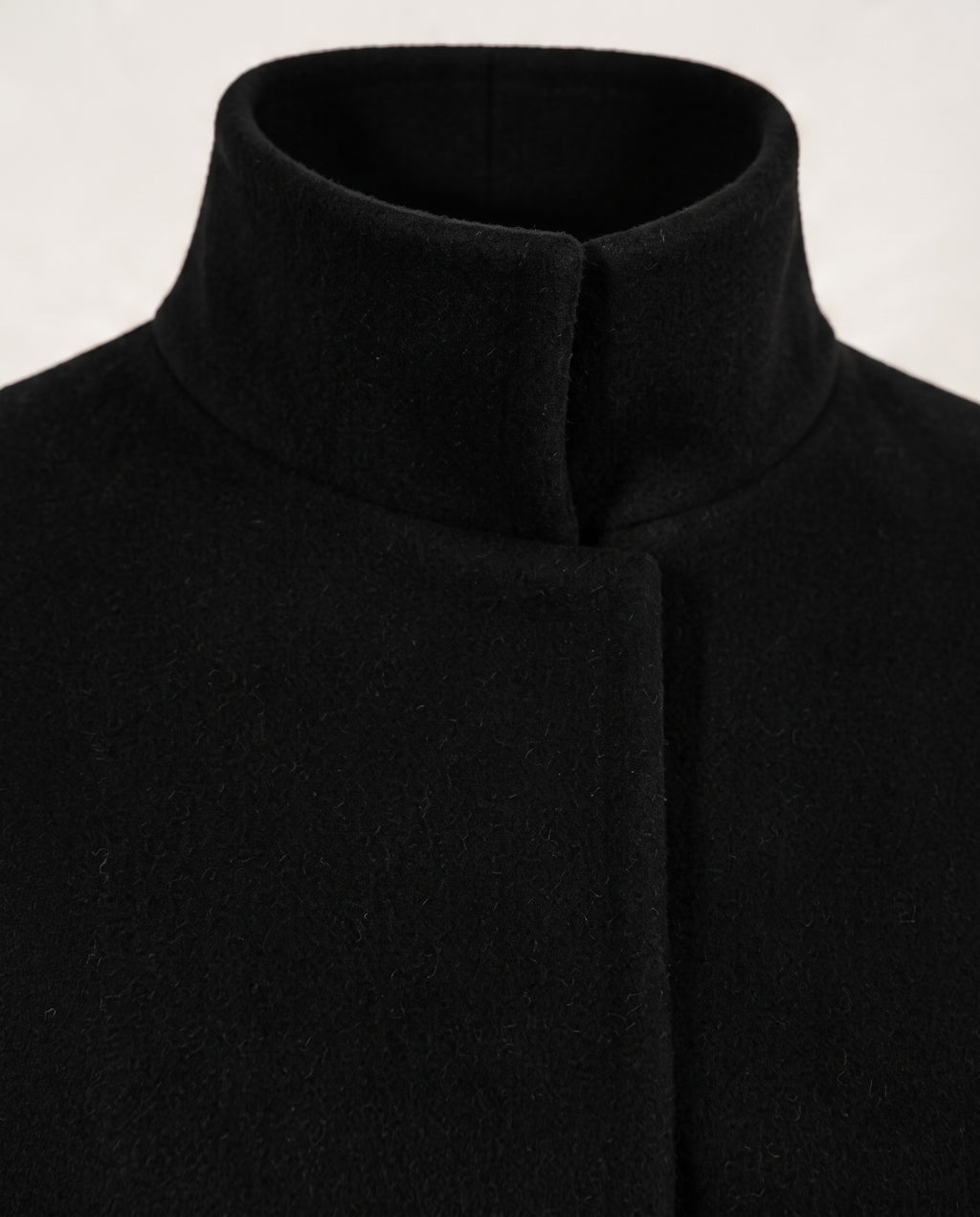Close-up of a black high-neck coat or sweater with a wide collar and front closure, shown against a plain light background.