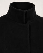 Close-up of a black high-neck coat or sweater with a wide collar and front closure, shown against a plain light background.