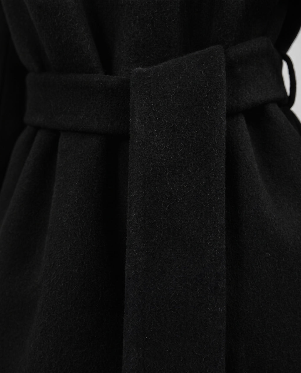 Close-up of a black belted coat or dress fabric, showing the waist tie and soft textured material.