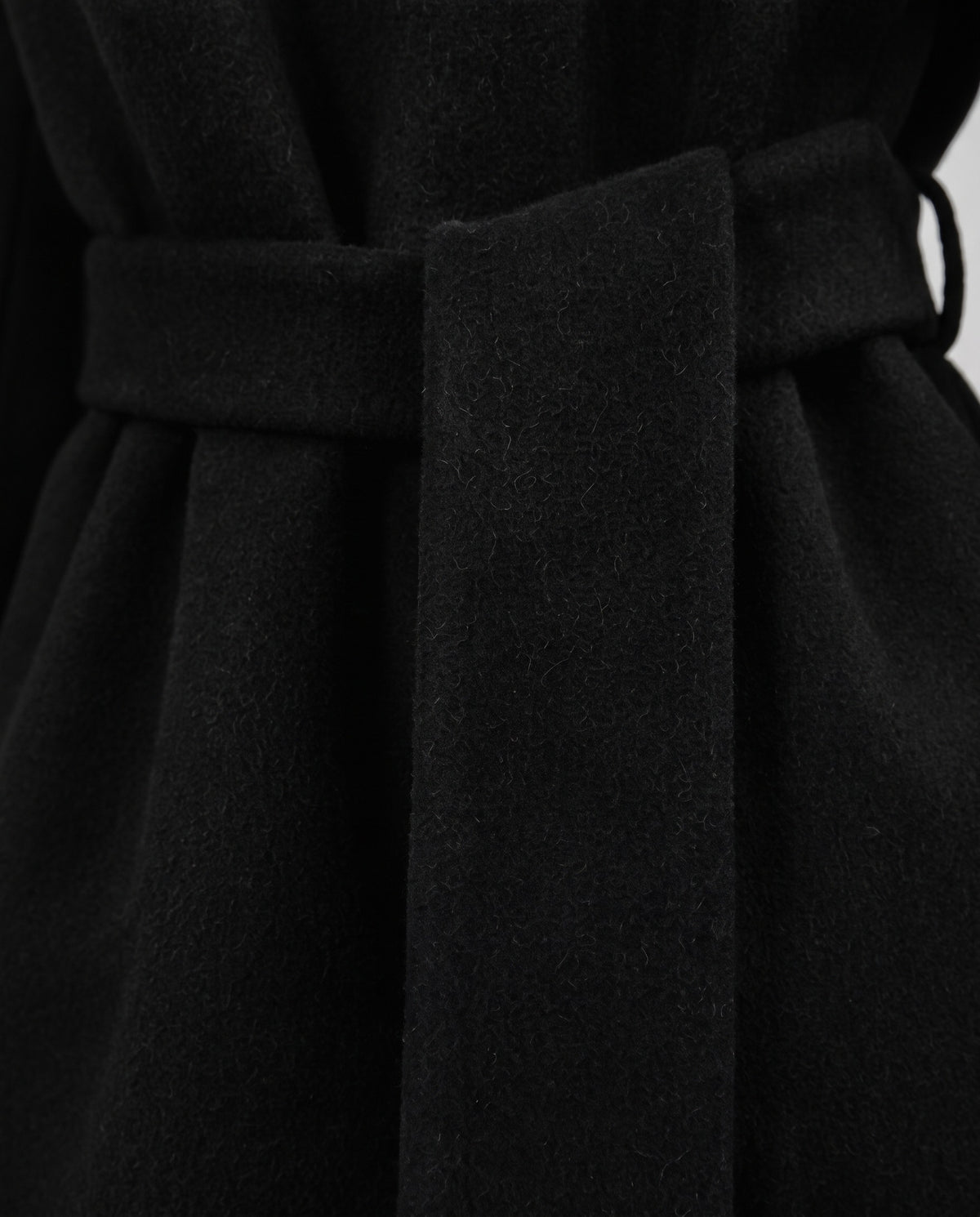 Close-up of a black belted coat or dress fabric, showing the waist tie and soft textured material.