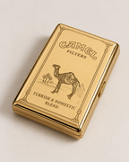 A gold Camel Filters tin box on a light beige background, featuring the classic camel logo and 'Turkish & Domestic Blend' text.