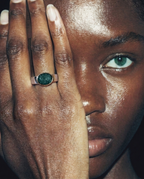 Close-up of a person's hand with a ring featuring a green gemstone, held near the face.