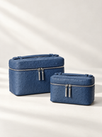 Two blue textured cosmetic bags with silver zippers, one larger rectangular bag and one smaller rounded rectangular bag, displayed on a light beige background with soft diagonal shadows.
