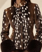 A close-up of a woman wearing a brown faux fur jacket with a white spotted deer print, featuring a mock neck, three brown buttons, and dark brown faux fur cuffs.