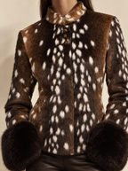 A close-up of a woman wearing a brown faux-fur jacket with a white spotted deer-antler pattern, featuring a high collar, buttoned front, and matching dark brown faux-fur cuffs.