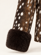 Close-up of a brown faux fur garment with white spotted pattern and a thick dark brown fur cuff, shown against a plain off-white background.