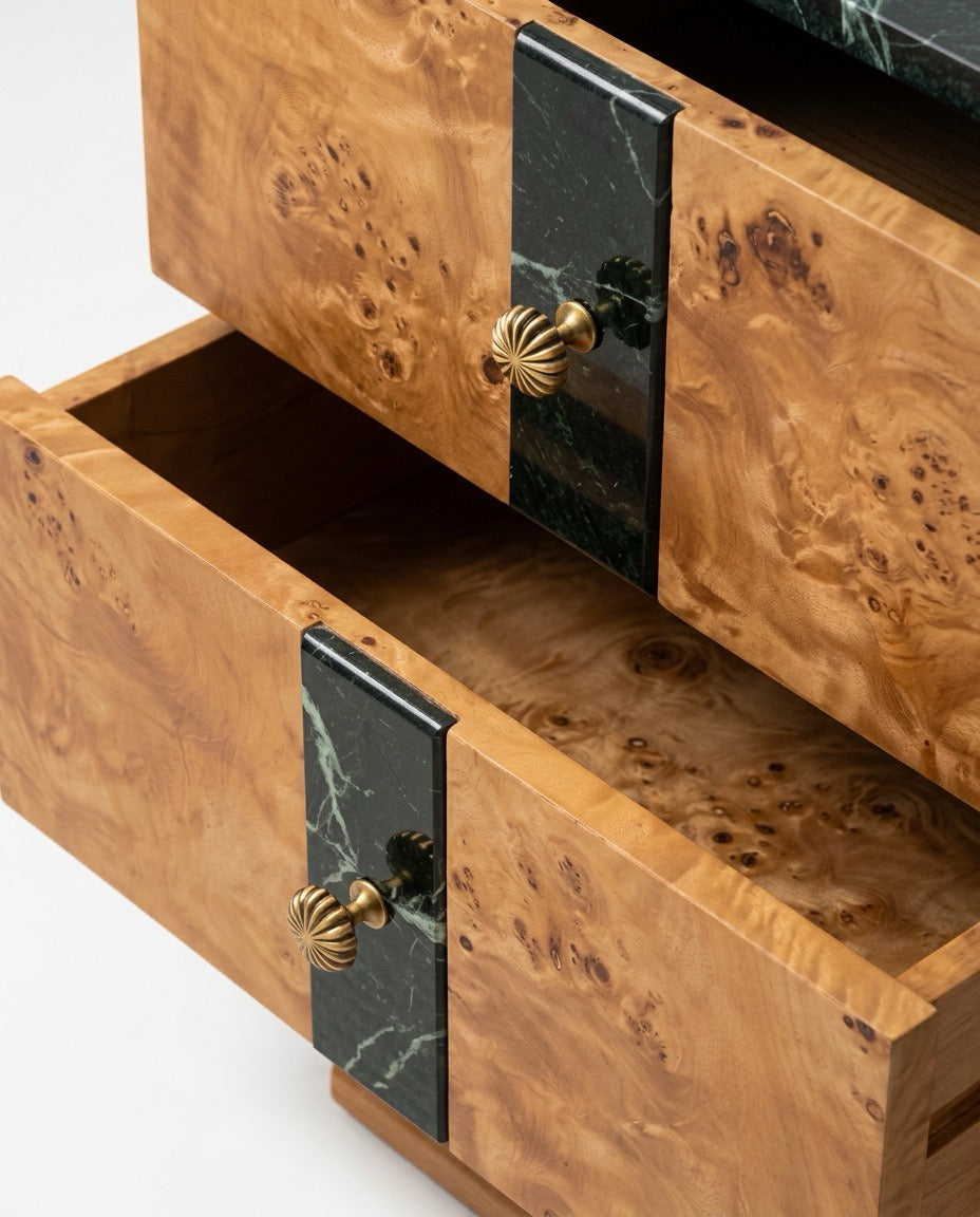 Close-up of a wooden chest of drawers with burl wood grain, black marble drawer pulls, and brass knobs, with one drawer open to show the interior.
