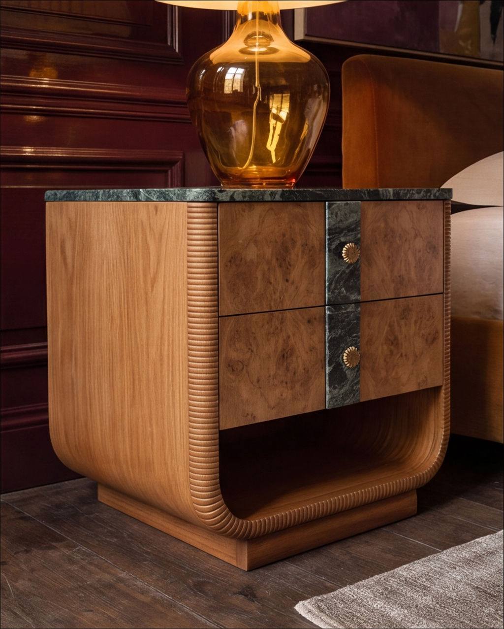 A luxury nightstand with a sculptural curved frame, burl wood grain, ribbed details, and a dark green marble top, styled in a bedroom setting with a glowing amber glass lamp on top.