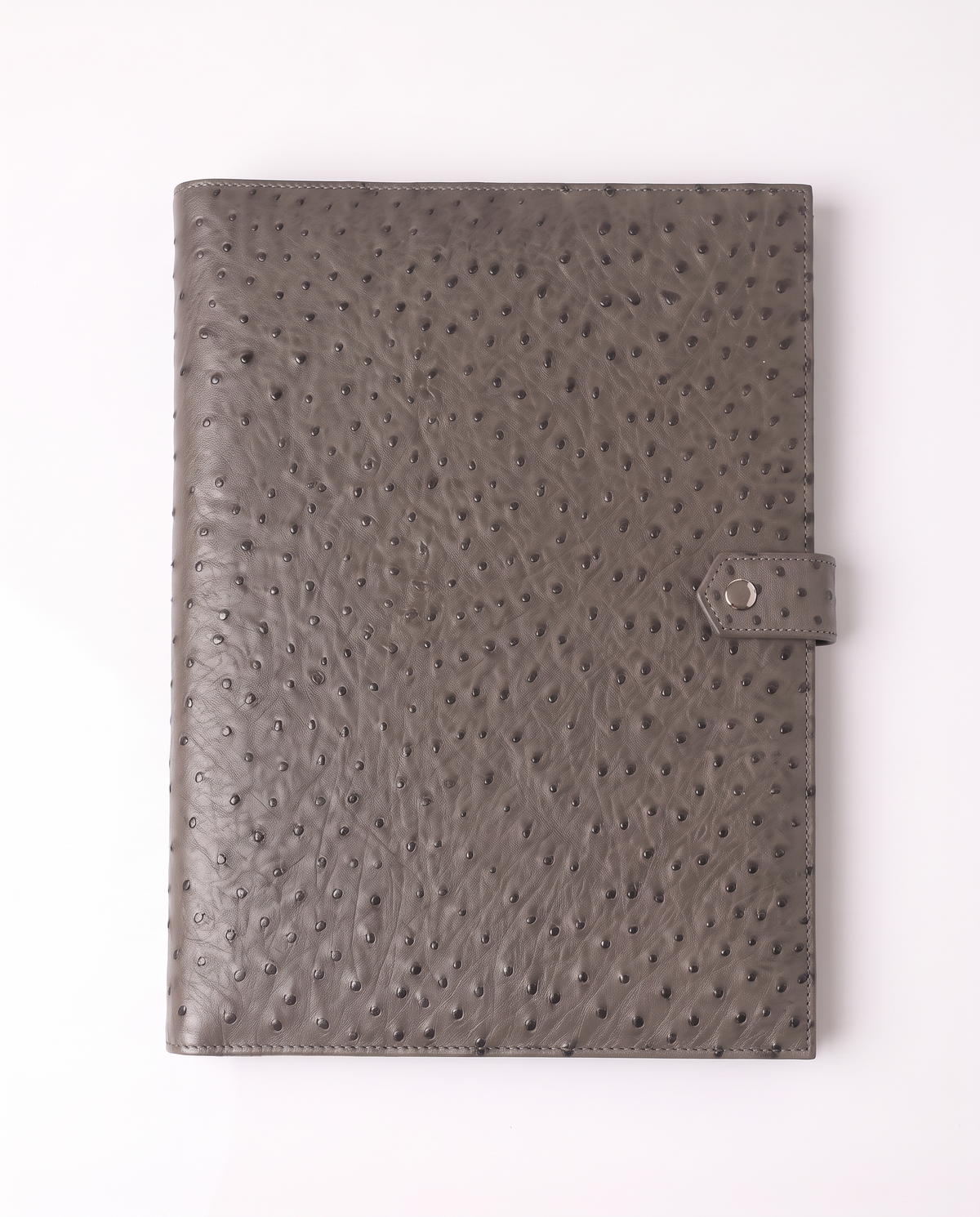A gray ostrich-textured leather notebook cover with a side strap and snap button closure, photographed flat against a clean white background.