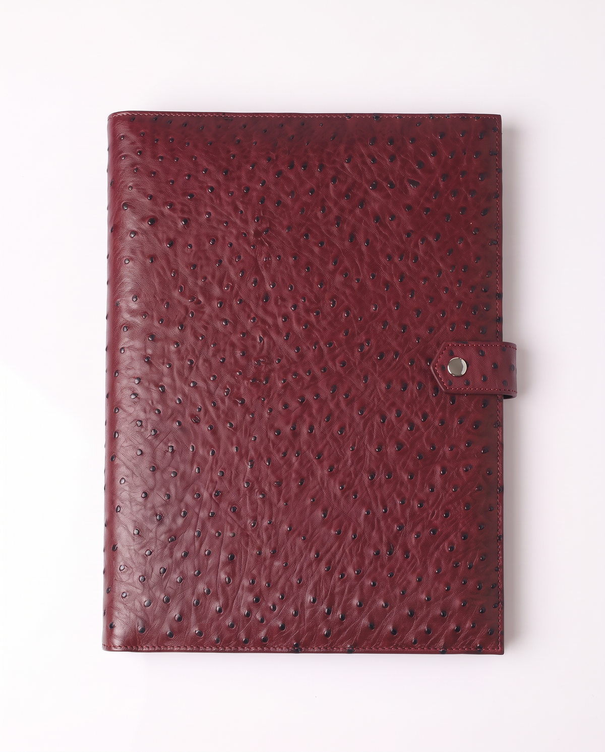 A burgundy ostrich leather notebook or planner cover with a snap-button strap closure, shown flat against a clean white background.