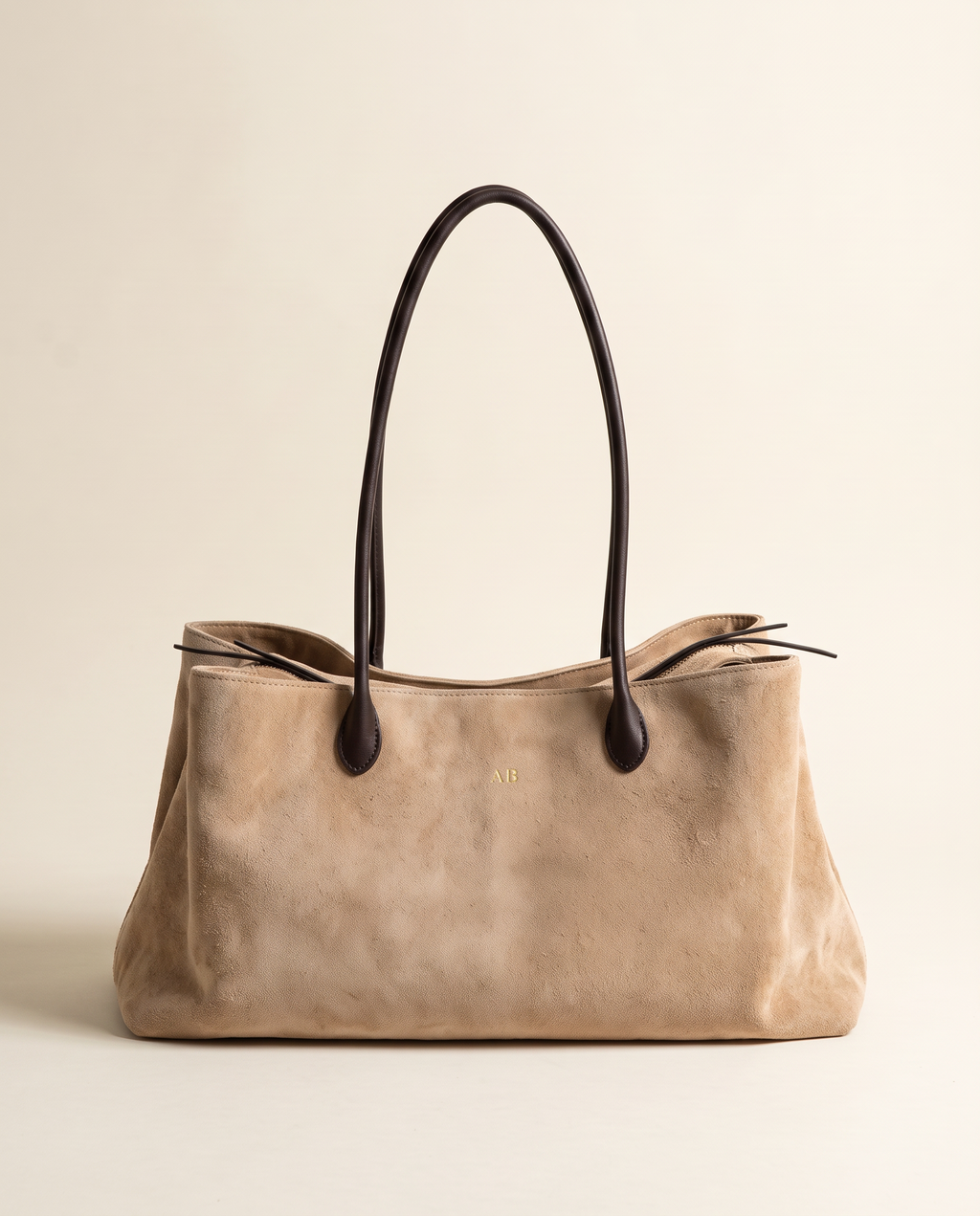 The Marais Tote in Apricot suede with dark leather handles, monogrammed with gold initials on the front