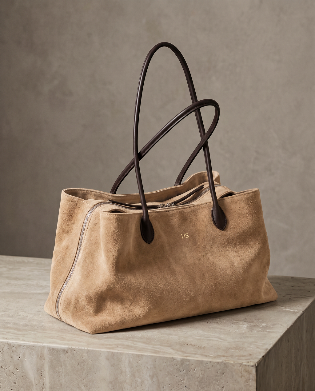 The Marais Tote in Apricot suede on a stone plinth, with gold embossed initials