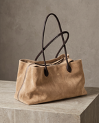The Marais Tote in Apricot suede on a stone plinth, with gold embossed initials