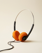 Over-ear wired headphones with bright orange foam ear cushions and a black headband, photographed on a clean warm beige background.