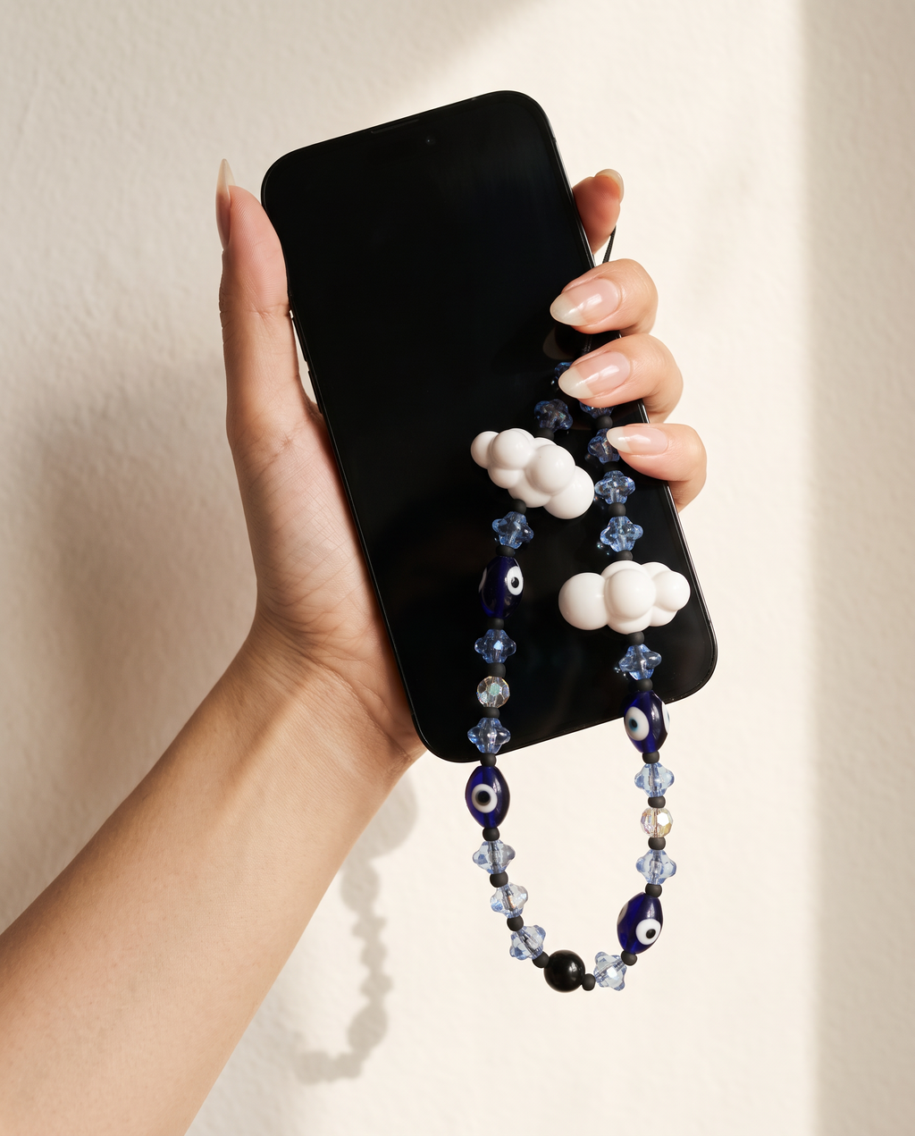 A hand holding a phone with The Daydream Phone Strap looped below