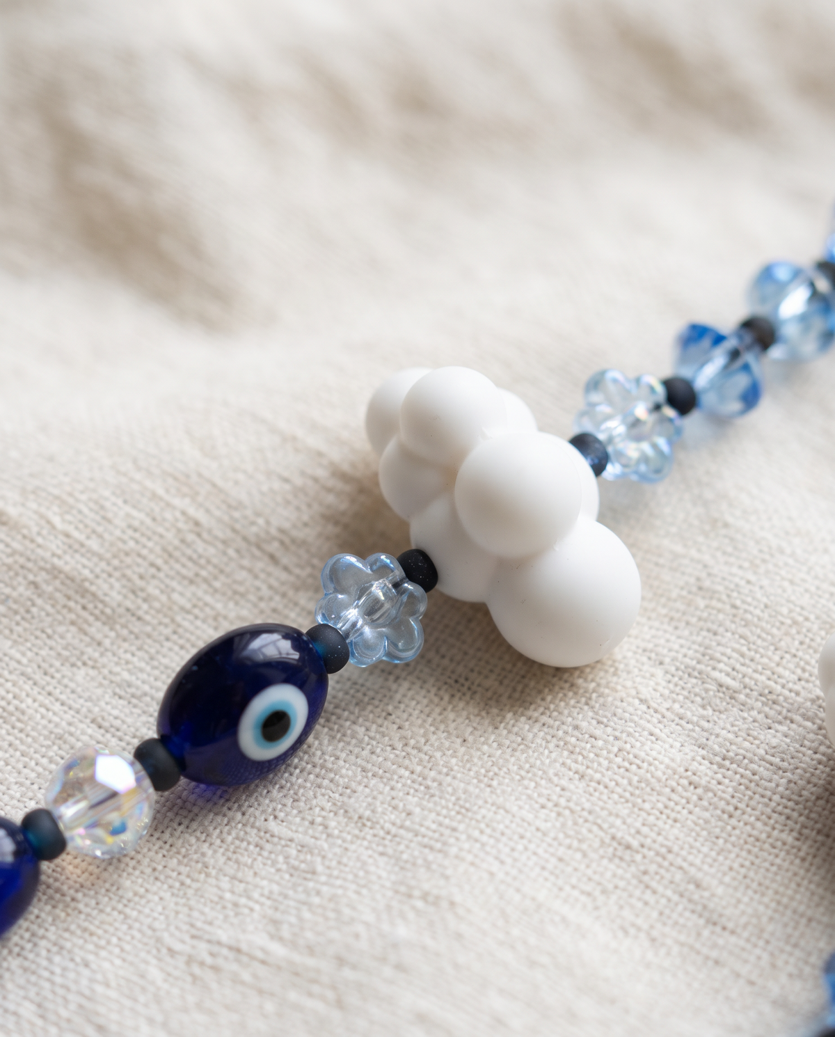 Close-up of a white cloud charm, pale blue flower beads and a navy evil eye bead