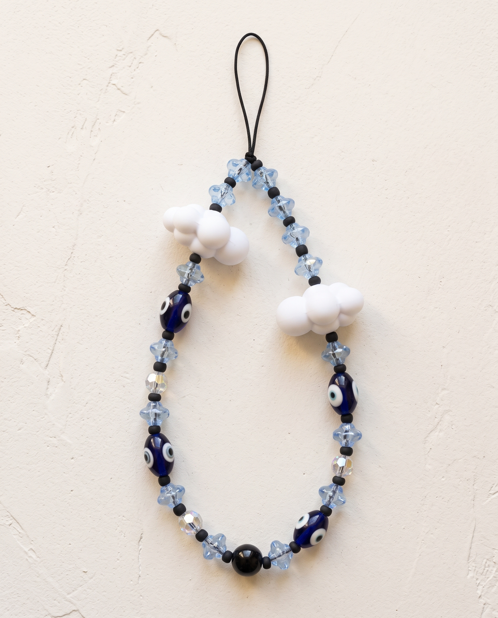 The Daydream Phone Strap laid flat: pale blue flower beads, navy evil eye beads and two white cloud charms