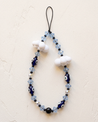 The Daydream Phone Strap laid flat: pale blue flower beads, navy evil eye beads and two white cloud charms