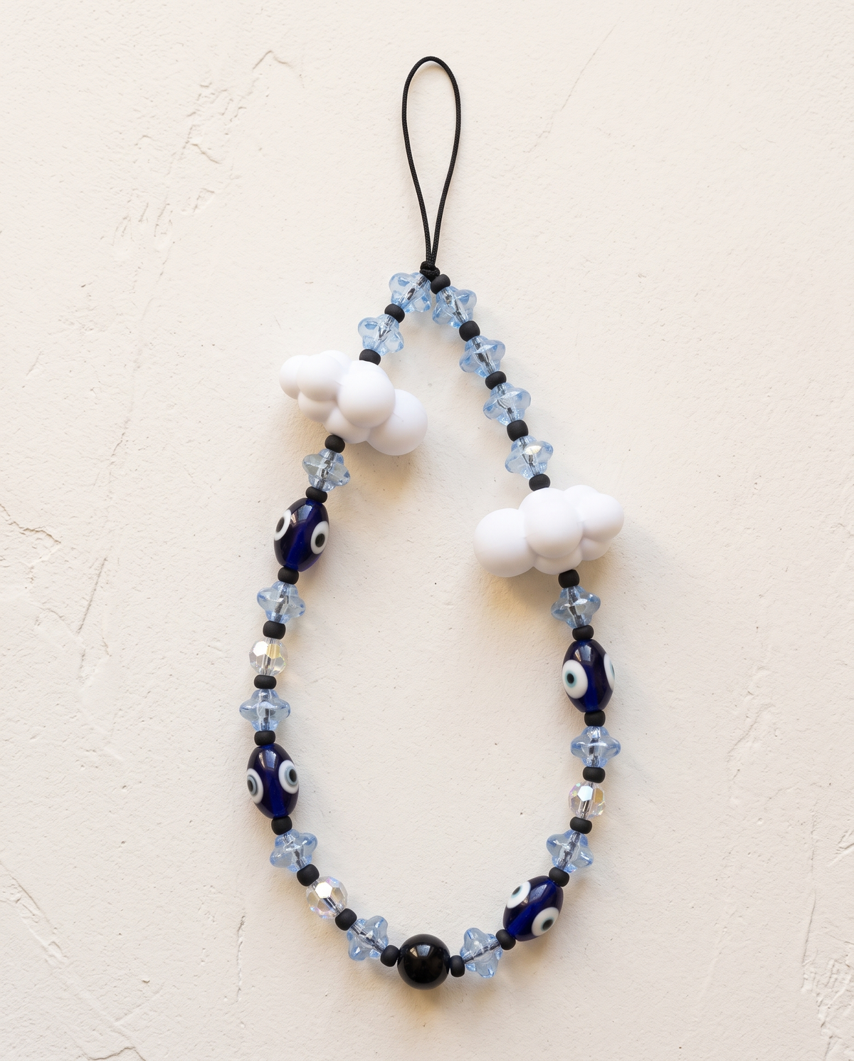 The Daydream Phone Strap laid flat: pale blue flower beads, navy evil eye beads and two white cloud charms