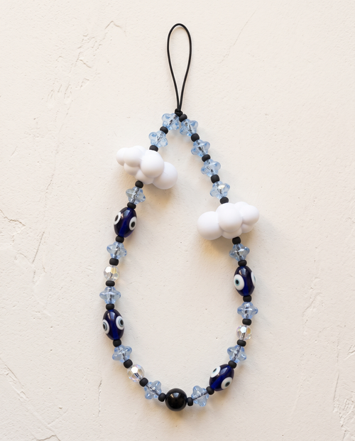 The Daydream Phone Strap laid flat: pale blue flower beads, navy evil eye beads and two white cloud charms