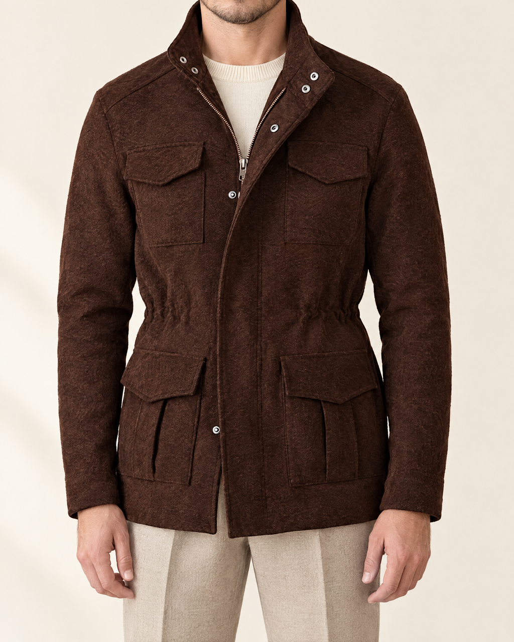 A man wearing a dark brown textured wool-blend jacket with a stand collar, front zipper, and four front flap pockets, styled over a cream knit sweater and beige trousers.