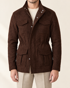 A man wearing a dark brown textured wool-blend jacket with a stand collar, front zipper, and four front flap pockets, styled over a cream knit sweater and beige trousers.