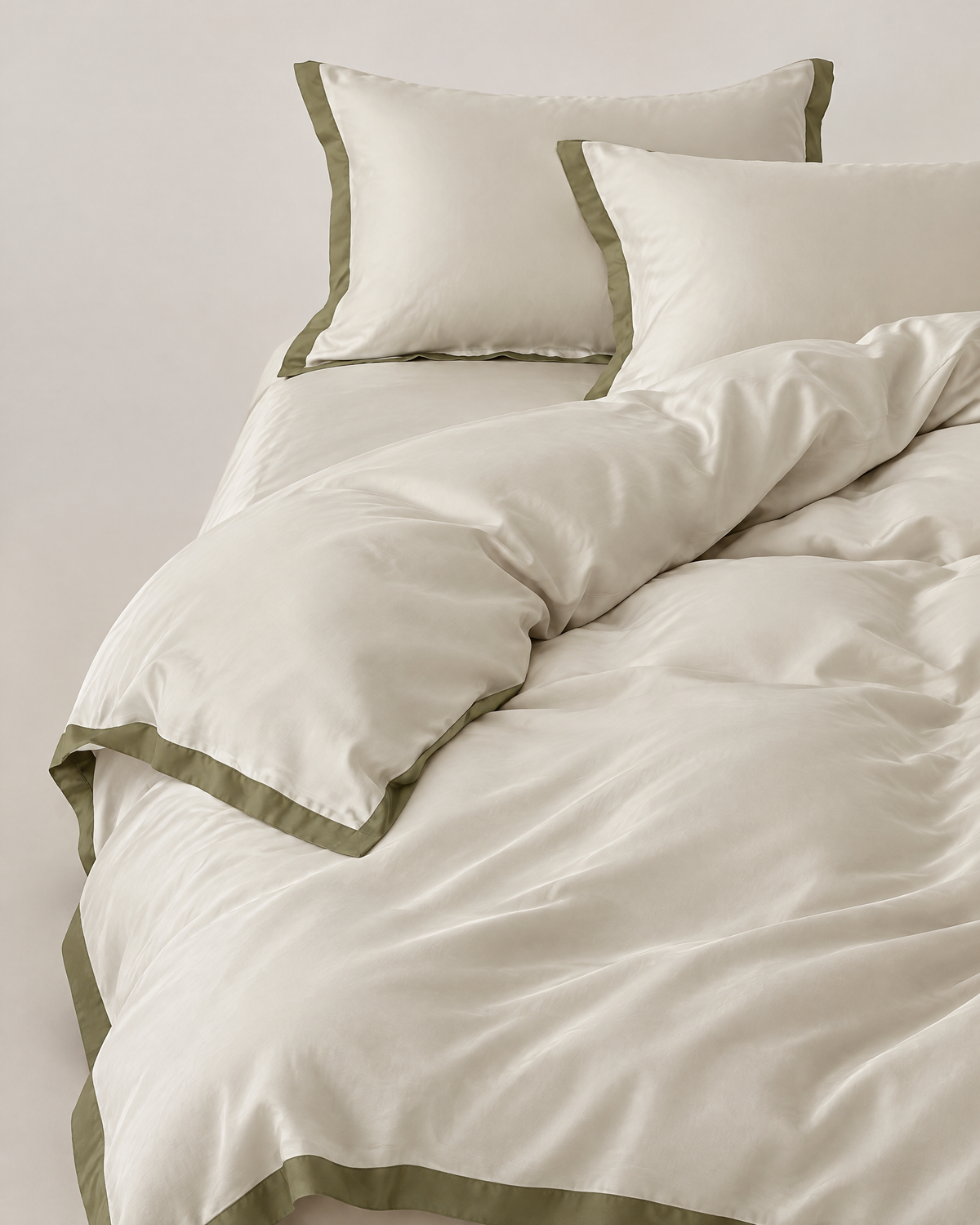 The Lyon Silk Bedding Set in ivory with olive border, unmade