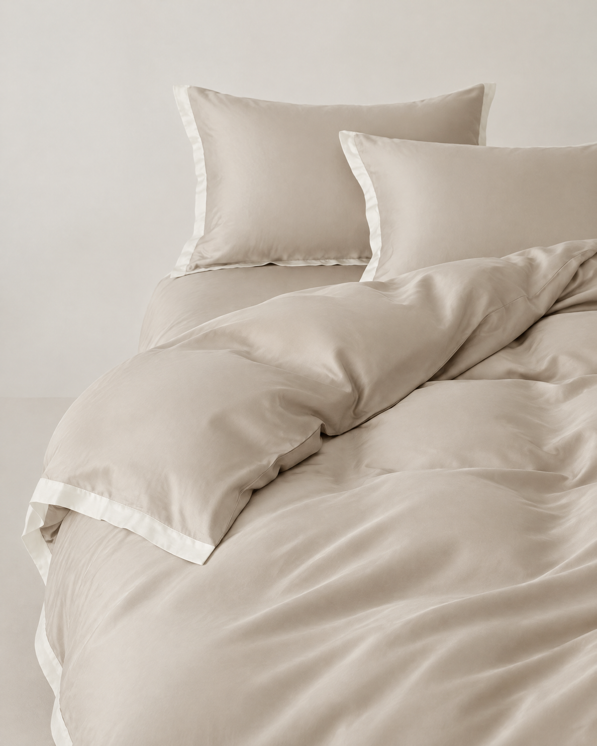 The Lyon Silk Bedding Set in oyster with ivory border, unmade