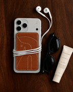 The Gallop Card Holder in stitched horse tan on the back of a phone, on a walnut table