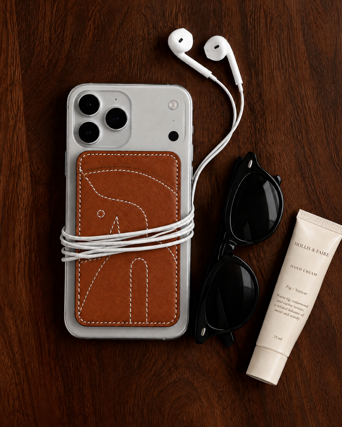 The Gallop Card Holder in stitched horse tan on the back of a phone, on a walnut table
