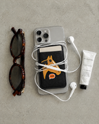 The Gallop Card Holder in horse patch black on the back of a phone, holding a card, with earphones, sunglasses and hand cream