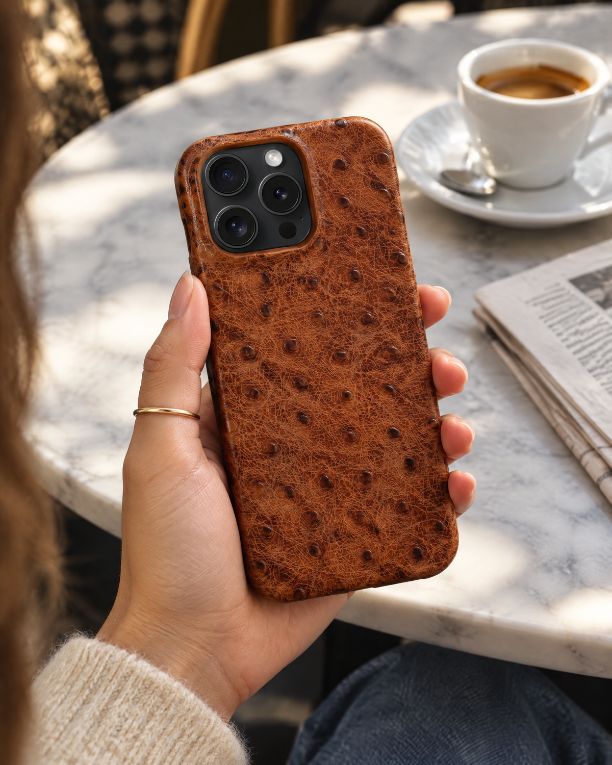 The Safari Phone Case in cognac brown, held at a marble cafe table