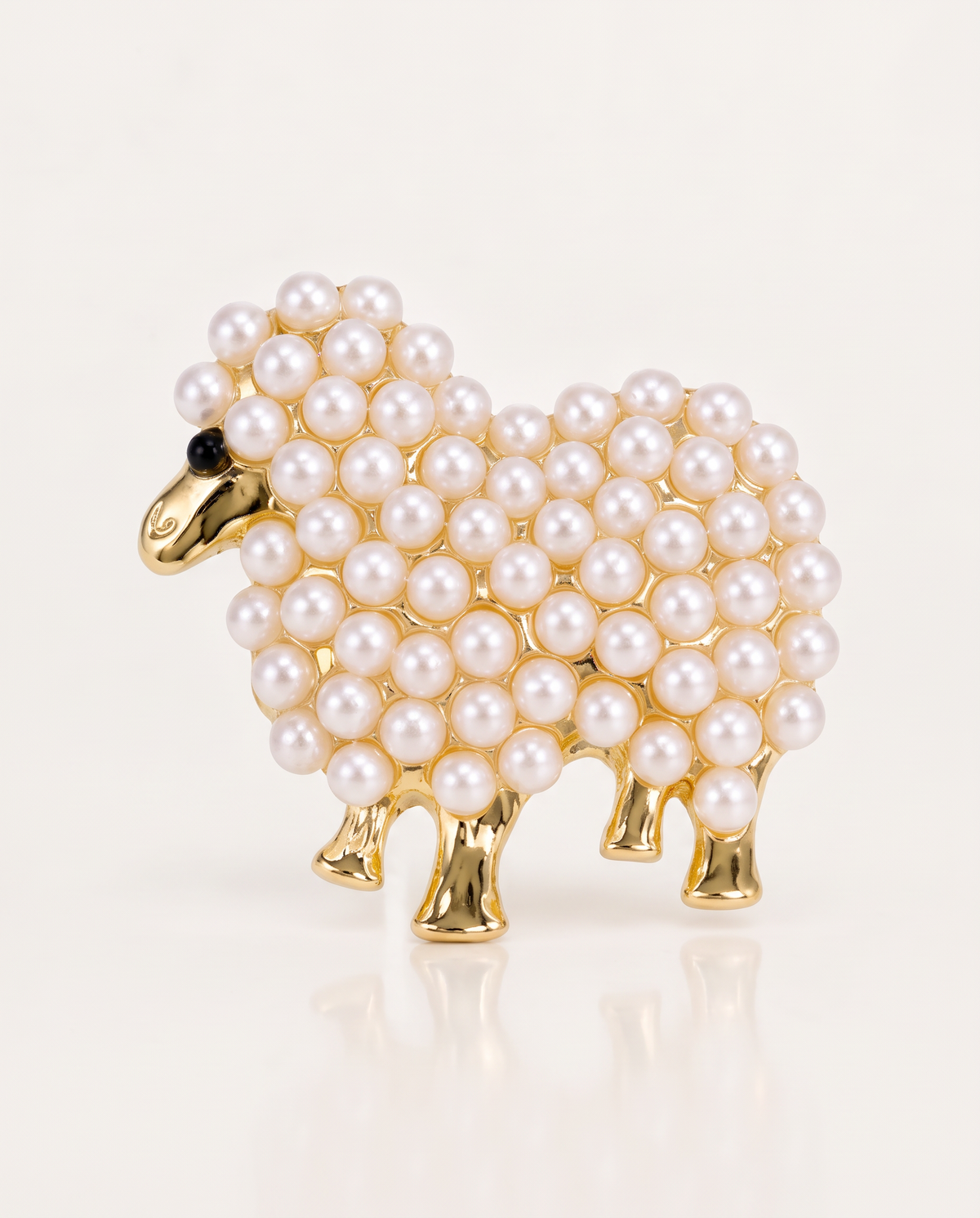 The Pearl Lamb Brooch in gold with pearl beads on an off-white background