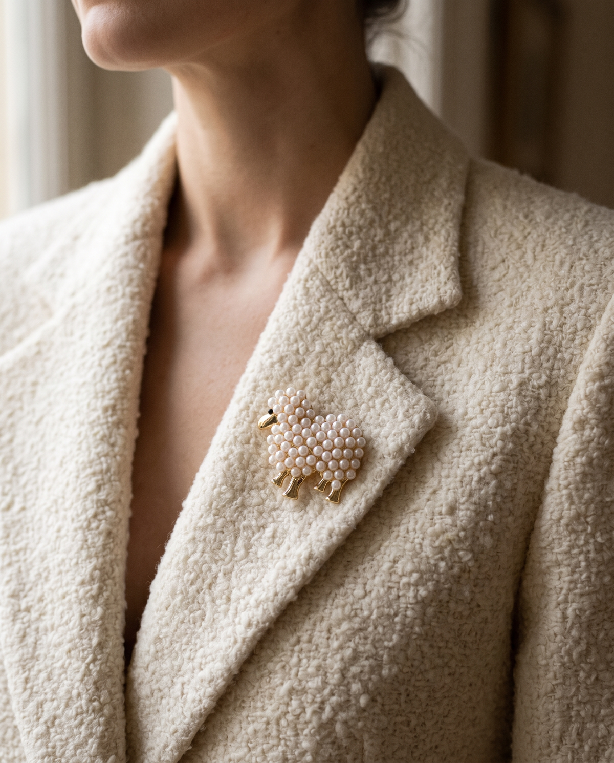 The Pearl Lamb Brooch worn on the lapel of a cream boucle blazer