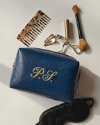A blue croc-embossed cosmetic bag with gold 'P.S.