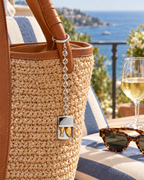 The Portofino Sardine Charm on a raffia tote on a Riviera terrace