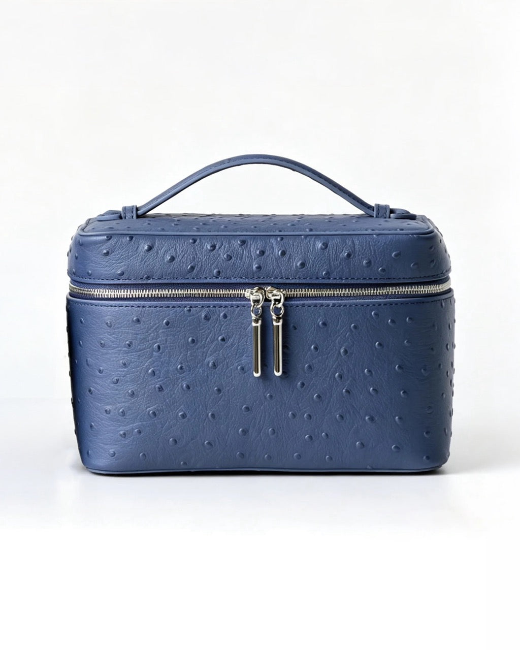 A blue ostrich-textured leather cosmetic case with a top handle, silver zipper, and dual zipper pulls, photographed on a clean white background.