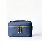 A blue ostrich-textured leather cosmetic case with a top handle and silver-tone zipper pulls, photographed against a clean white background.