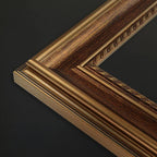 Close-up of a decorative picture frame corner showing layered woodgrain in dark brown and warm gold tones against a dark background.