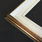 Close-up of a picture frame corner showing a textured gold frame, white matting, and a black background.