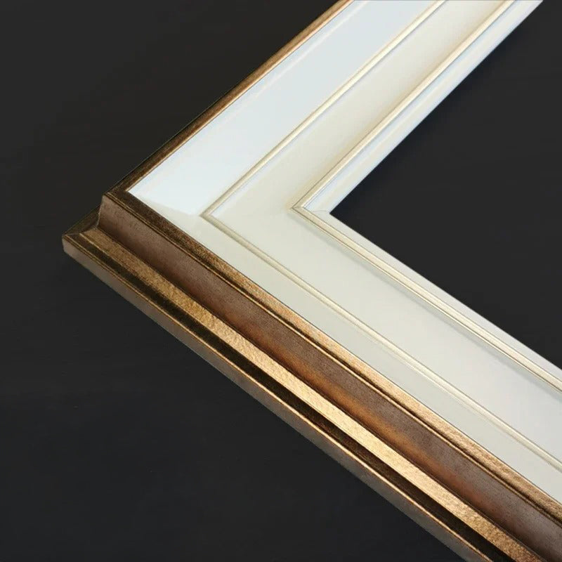 Close-up of a picture frame corner showing a textured gold frame, white matting, and a black background.