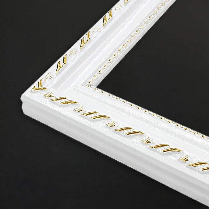 A close-up of a white decorative picture frame corner with gold embossed detailing, set against a solid black background.
