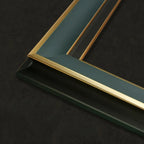 Close-up of a picture frame corner with a dark teal-green background and a polished gold inner border, set against a dark textured backdrop.